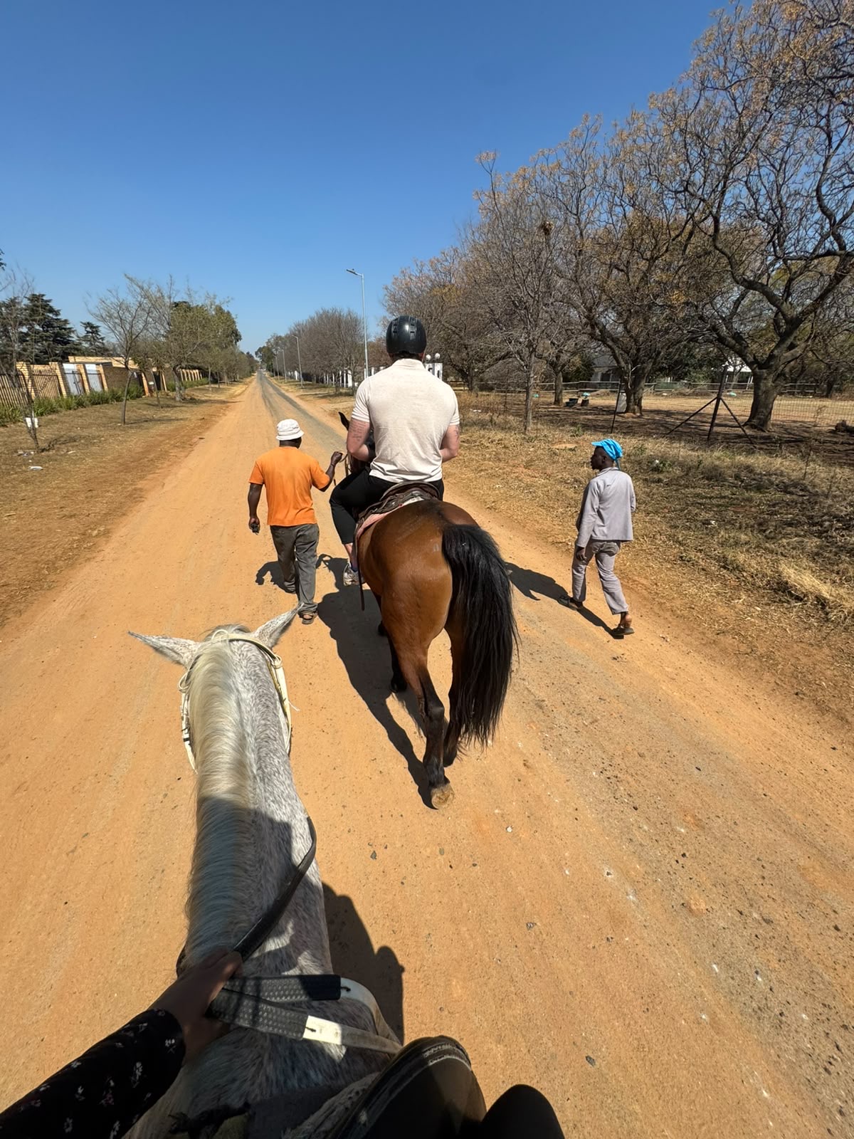 Two riders and grooms heading down a dirt road on an outride